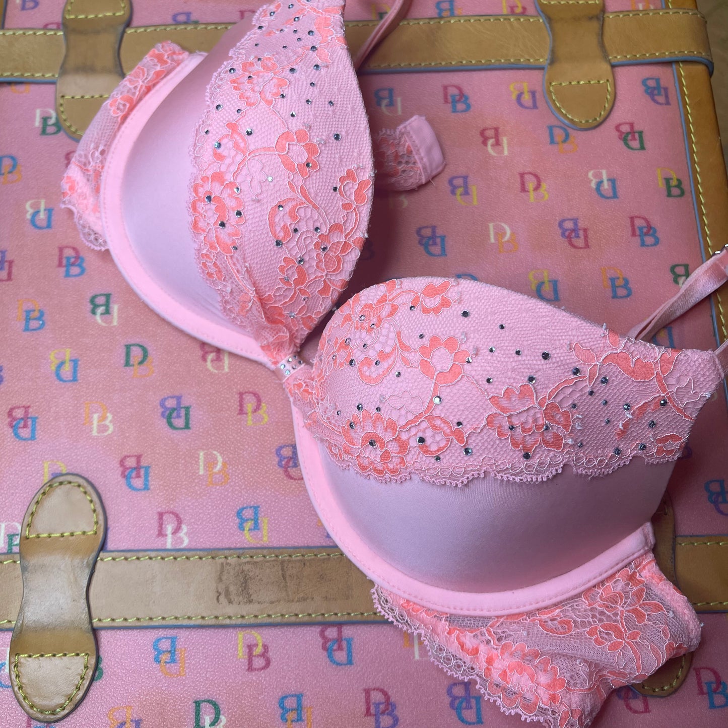 Pink Y2k Victoria’s Secret Bra with Lace and Rhinestones sits on top of a pink D&B suitcase